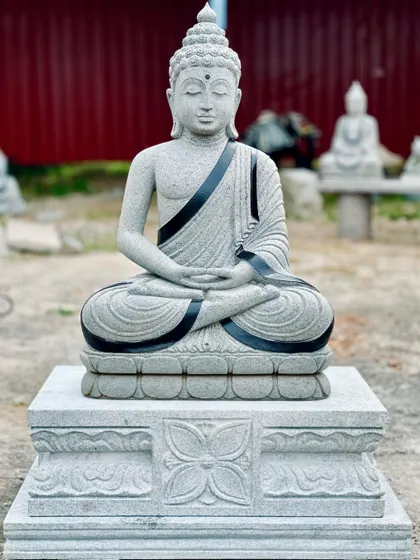 A serene stone Buddha statue on a carved pedestal, perfect for creating a meditation corner in a garden.