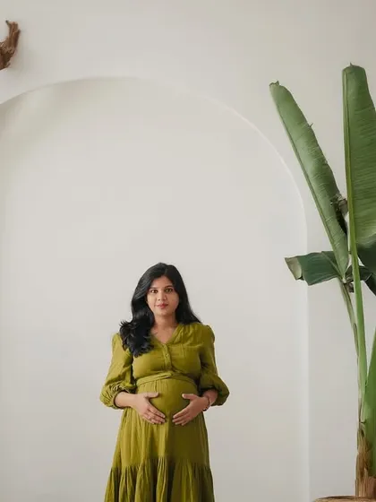 A minimalist and modern studio portrait. The clean white arch, natural wood, and green plant create a fresh and organic backdrop for the mother-to-be.