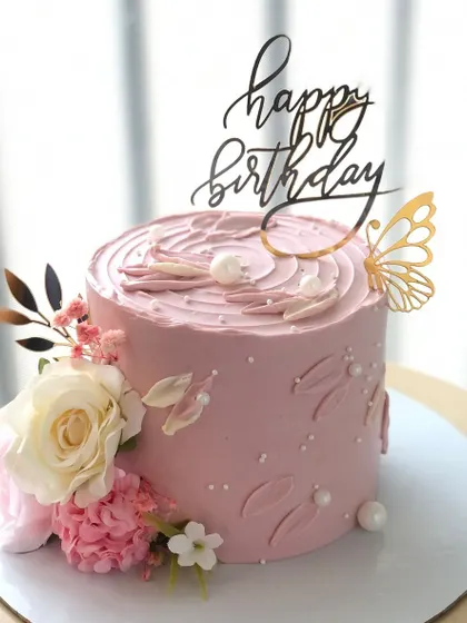 An elegant pink cake with fresh flowers and a golden butterfly accent.