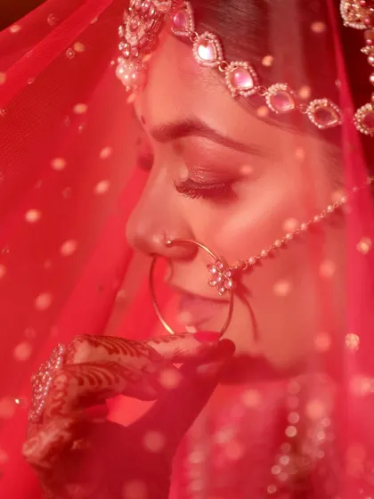A close-up shot of a bride through her red veil, focusing on her traditional nath (nose ring). This intimate and artistic photo highlights a key element of the bridal look.