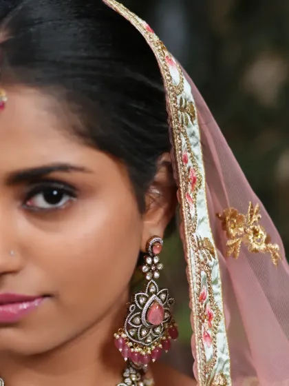 A half-face close-up focusing on the exquisite earring, with its intricate metalwork and beautiful pink stones.