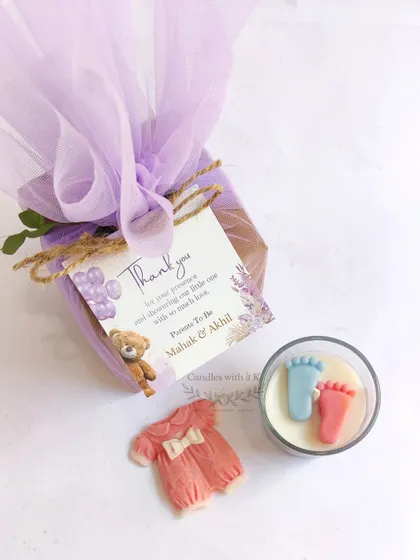A beautiful baby shower gift set featuring a layered votive candle and a baby onesie wax sachet, showing the complete packaged favor with its custom tag.