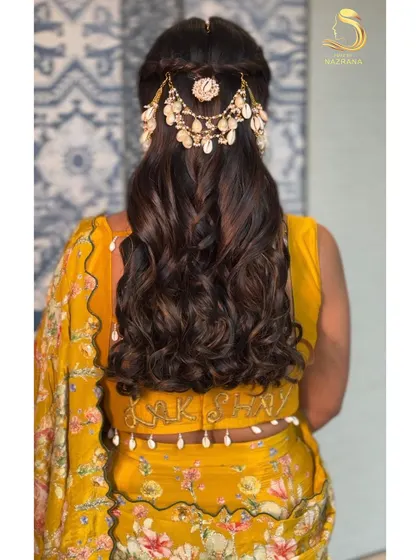 The back view of this beautiful Haldi hairstyle, complete with braids and a unique hair accessory made of shells and pearls.