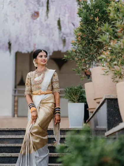 A full-length view of a stunning bride in her off-white and gold Kanjivaram saree. The makeup is kept elegant and natural to let the richness of her attire shine.