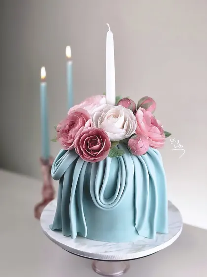 An elegant blue cake with a fondant drape effect and a beautiful bouquet of pink and white sugar flowers.