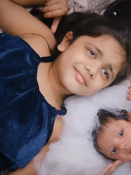 A beautiful portrait of sibling love. The older sister looks on protectively as her newborn sibling rests beside her.