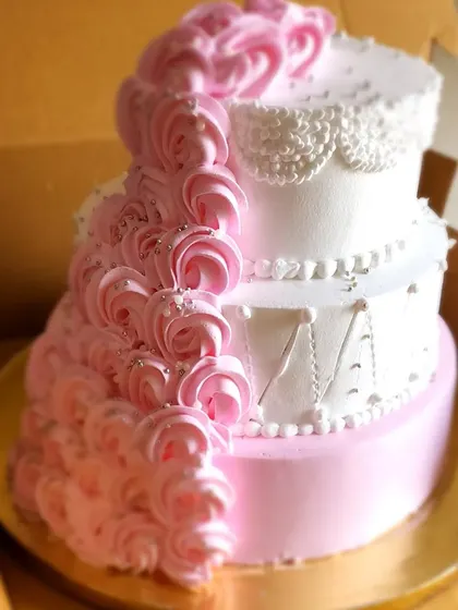 An elegant three-tier engagement cake ready to join the party. The design features a cascade of pink buttercream rosettes and delicate lace-like piping, combining classic and modern styles.