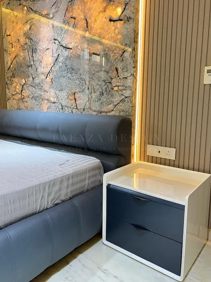 A close-up of the custom bed and bedside table. The navy blue drawers of the nightstand contrast beautifully with the white frame, and the backlit marble-effect panel adds a warm, ambient glow.