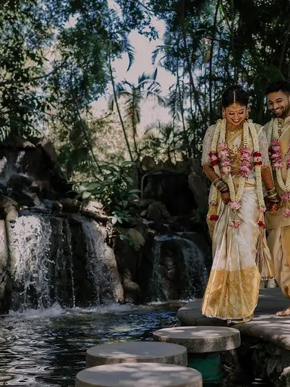 The couple takes a walk by the waterfall, a serene moment on their wedding day. The bride's classic white and gold saree and my soft makeup application look absolutely timeless in this beautiful setting.