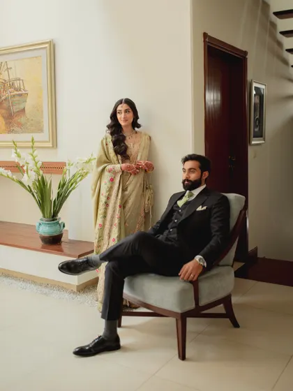 Modern love with a touch of classic style. This portrait captures the couple in a chic indoor setting, with the groom seated and the bride standing behind him, creating a look that is both fashionable and intimate.