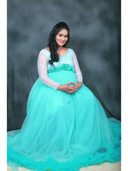 A seated portrait in the cyan maternity gown, showing the comfortable fit and the floral detail on the waist belt.