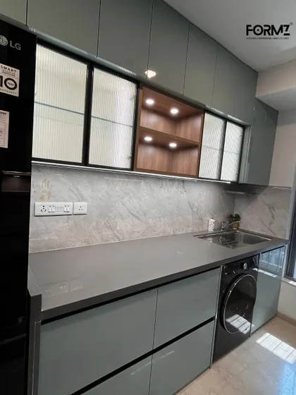 A combination of fluted glass and open wooden shelving provides both concealed and display storage. The warm light from the open shelf contrasts beautifully with the cool tones of the grey cabinets and marble-patterned backsplash.
