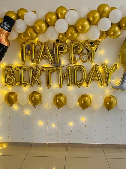 A fun birthday decoration for an adult, featuring gold and white balloons and foil balloons shaped like a whiskey bottle and a glass.