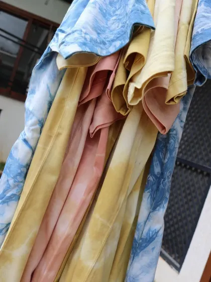 A cascade of colorful, naturally dyed t-shirts. The different hues of blue, pink, and yellow show the beautiful range of colors that can be achieved from nature.