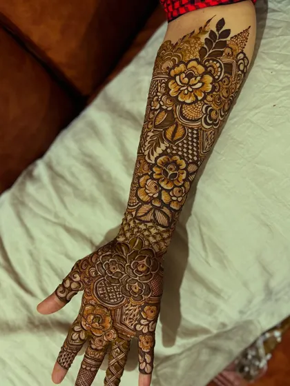 A single arm view of a detailed floral henna design, showing the flow of the pattern from the hand to the elbow.