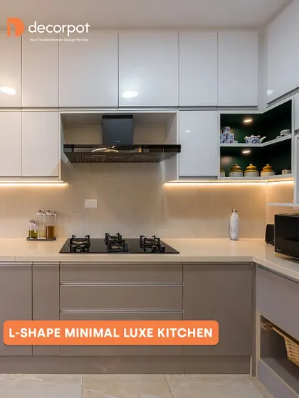 The 'Minimal Luxe' L-shaped kitchen combines soft beige lower cabinets with crisp white upper ones. We added a pop of color with a dark green open-shelf unit, creating a subtle yet stylish focal point in this elegant design.