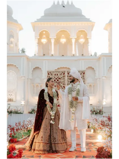 A candid moment of laughter between the couple on their wedding stage, set against a magnificent white architectural backdrop.