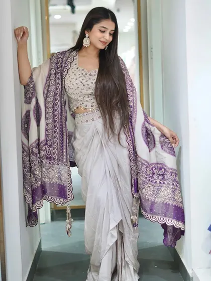 This Dhoti Blouse Cape Set is perfect for wedding functions. The off-white dhoti pants are paired with a beautifully embroidered blouse and a purple printed cape.