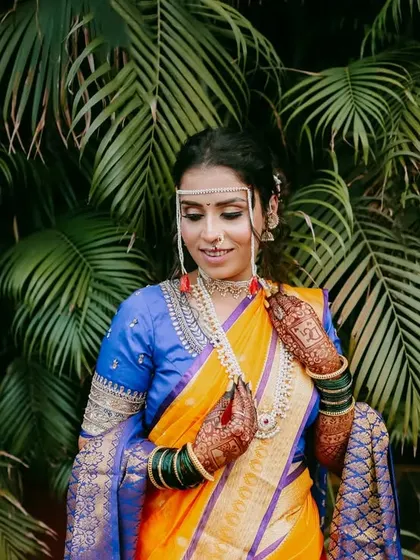 A beautiful portrait of a Maharashtrian bride against a backdrop of lush palm leaves, highlighting the vibrant colors of her saree.