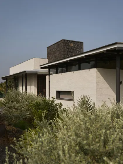 A view of Pavilion House, showing the contrast between the white brick, dark stone chimney, and the surrounding greenery.