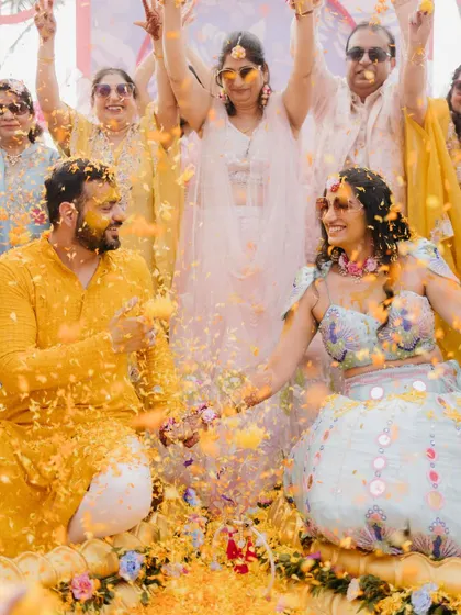 A joyous photo of the couple during their Haldi, surrounded by family who are showering them with flower petals.