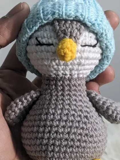 A tiny, sleepy penguin wearing a blue hat, held in my hand to show its small size.