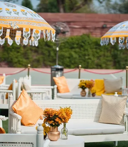 Comfortable lounge seating with vibrant orange cushions and traditional printed umbrellas at the Umaid Bhawan Palace Haldi.