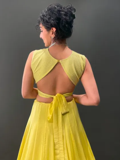 The back of this yellow blouse features a chic cut-out and tie-up detail, adding a playful and modern touch to the ensemble.
