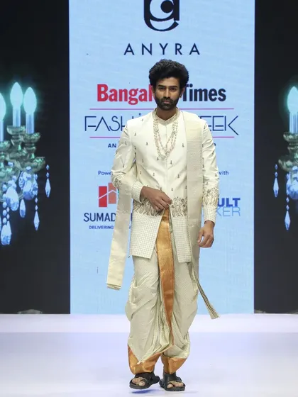 A front-facing runway view of the traditional silk dhoti and embroidered sherwani combination. The gold border on the dhoti is a classic detail that adds a touch of richness to the overall look.