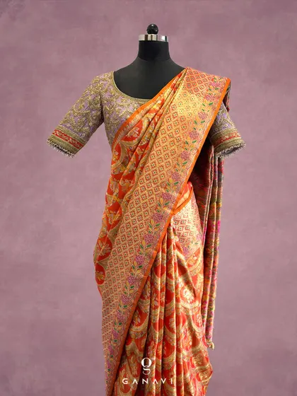 A beautiful orange and gold Banarasi silk saree paired with a custom lavender blouse. The blouse features heavy, jewelry-inspired embroidery, creating a stunning contrast and a truly unique bridal look.