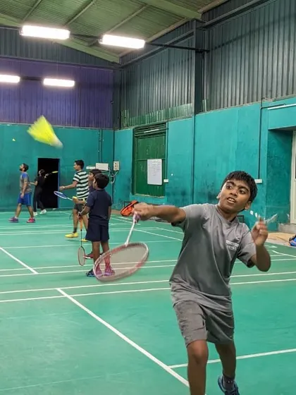 A young player makes contact with the shuttlecock during a practice match. We incorporate match play into our coaching to build tactical awareness.