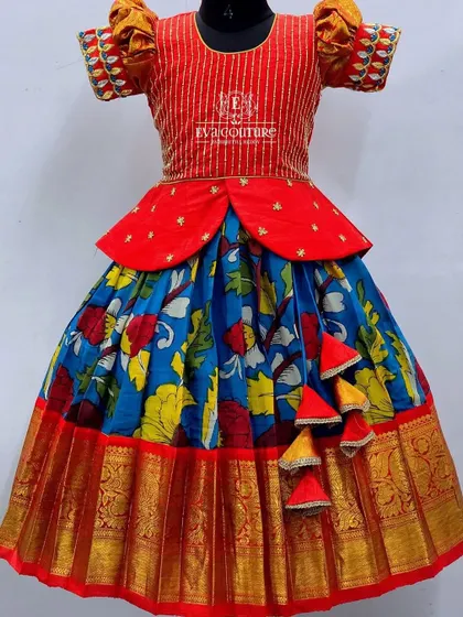 A colorful Kanchi pattu lehenga with a red peplum top. The blue skirt features a vibrant floral Kalamkari-style print, finished with a traditional red and gold border.