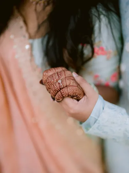 A close-up shot of the engagement ring being placed on the bride's mehendi-adorned hand.