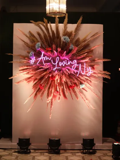 A unique photo wall made from dried pampas grass, with a personalized neon sign for the couple, creating a trendy and memorable spot for pictures.