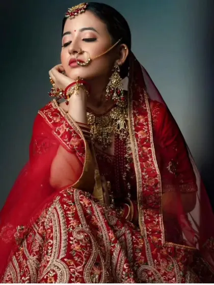 An artistic shot of a bride in a red lehenga, wearing a traditional red-beaded jewellery set. The pose highlights the delicate nath and jhumkas.