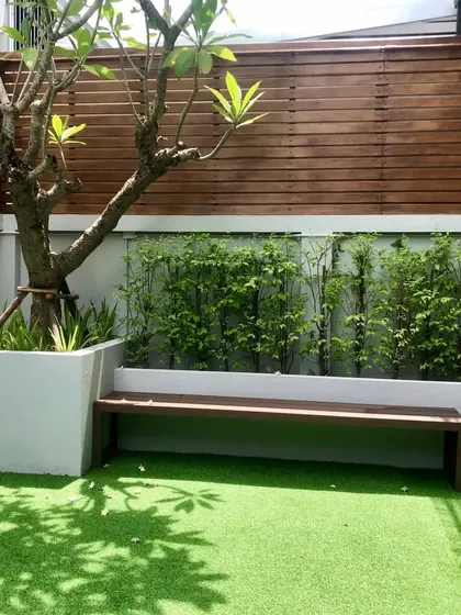 This cozy, shaded patio area combines a wooden bench and fence with a soft artificial grass floor. It’s a perfect example of creating a tranquil, low-maintenance garden retreat in a small space.