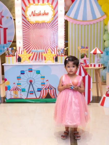 The birthday girl stands in front of her colorful circus-themed party decorations. Our event photography captures the bright and cheerful atmosphere of your child's celebration.