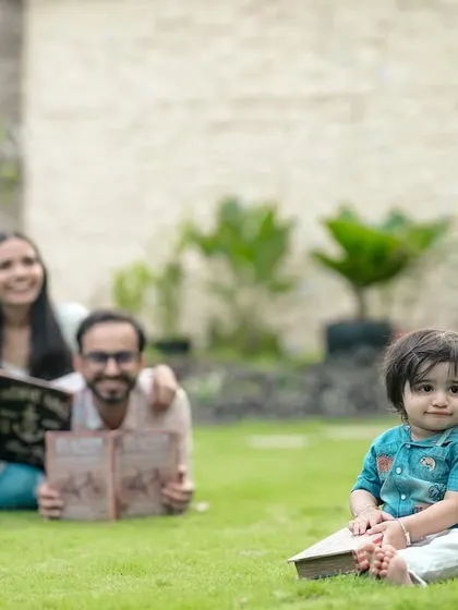 Story time on the lawn. This creative family portrait shows the parents enjoying a book together while their little one has his own, creating a fun and memorable outdoor photo.