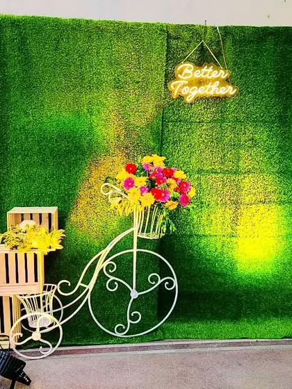 A simple yet beautiful backdrop for a pre-wedding event or anniversary. The green foliage wall with a "Better Together" neon sign and a decorative bicycle creates a rustic and charming atmosphere.