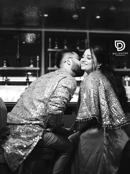 An artistic black and white photo of the groom kissing the bride's cheek, capturing a sweet, intimate moment during their engagement celebration.