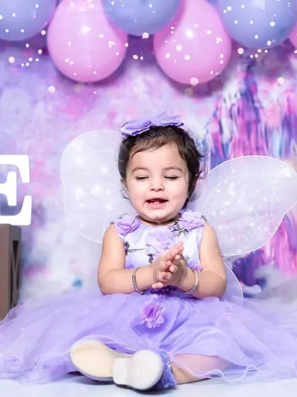 Mahira looks like a little angel in our fairy-themed setup. The purple dress, fairy wings, and dreamy castle background create a magical atmosphere for her first birthday photos.