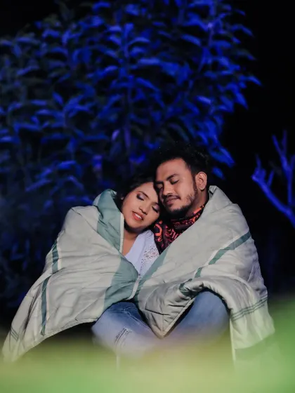 A quiet, intimate moment captured during a night-time pre-wedding shoot. The cool blue lighting and shared blanket create a feeling of warmth and togetherness.