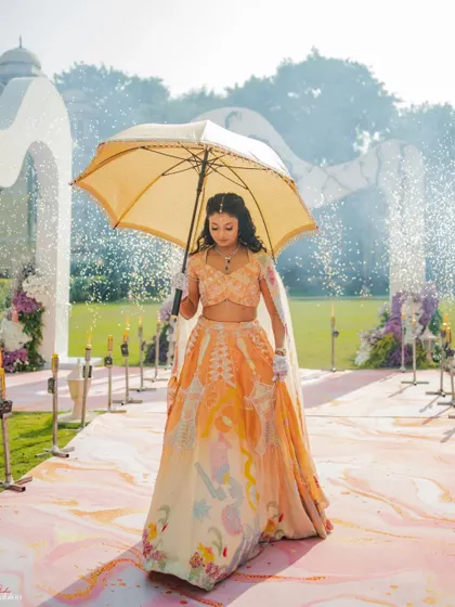The bride's grand entrance. This shot of Radhika walking under an umbrella, with a water fountain effect in the background, is a perfect example of a creative and dramatic bridal entry.