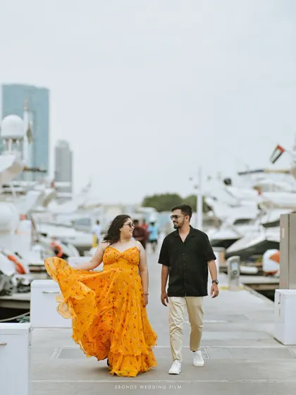 A candid walking shot of the couple at the Dubai marina, surrounded by luxury yachts. The focus is on their natural interaction and the grand scale of their surroundings.