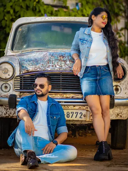 This pre-wedding photo captures a cool, casual vibe with the couple posing against a classic Indian car.