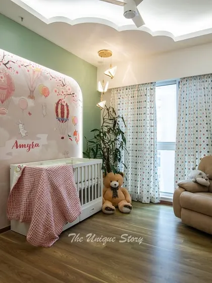 This nursery is a cozy and safe haven, featuring a white crib set against the whimsical mural. A comfortable recliner provides a perfect spot for feeding and bedtime stories, while the cloud-shaped false ceiling adds a touch of magic.