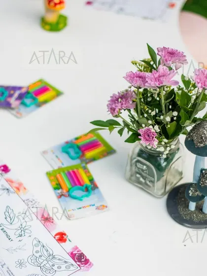 A table setting at a woodland party, complete with coloring activities for the kids. The small floral arrangement and mushroom prop tie in perfectly with the theme, showing that every detail is considered.