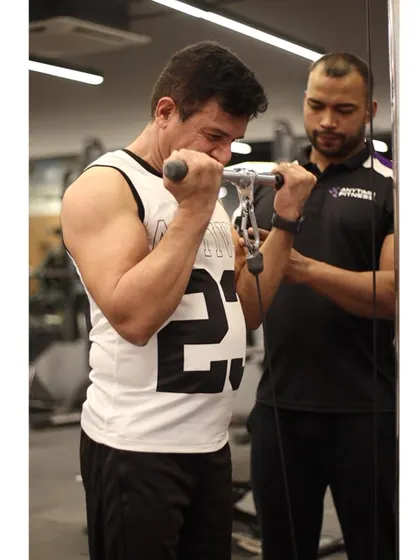A trainer provides spotting and encouragement to a member during a set of cable bicep curls, helping him push past his limits.
