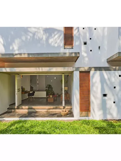 The ground floor of the Aayi House opens completely to the garden with large sliding glass doors. This design creates a seamless transition from the interior living space to the lawn, perfect for indoor-outdoor living in a tropical climate.