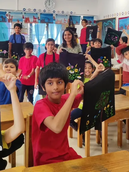 A vibrant classroom full of young students joyfully holding up tote bags they've painted with unique floral designs. This image captures the energy of a school workshop and the pride of creating a beautiful, usable piece of art.